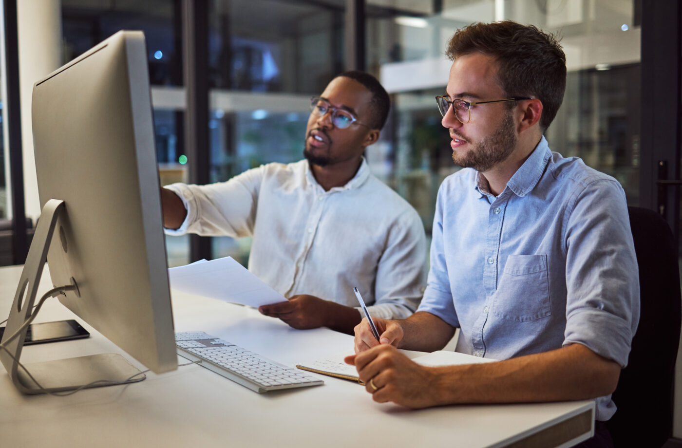 Two males sitting together at a desk looking at a computer screen