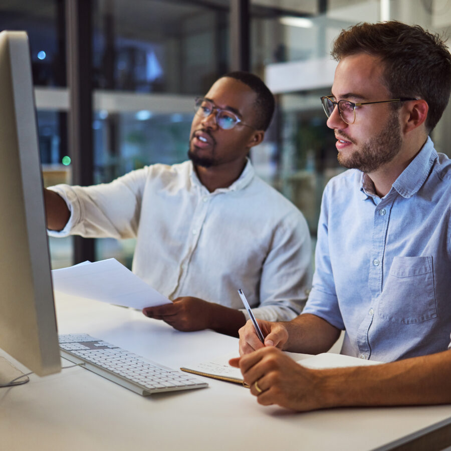 Two males sitting together at a desk looking at a computer screen