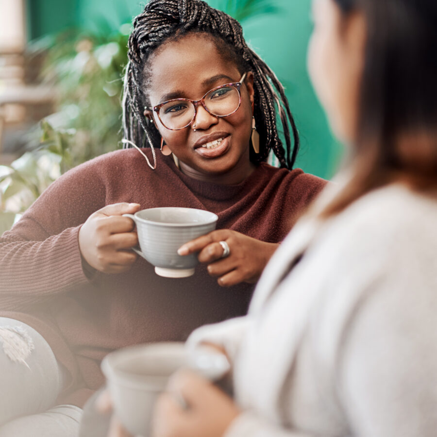 Two women sitting on a sofa having coffee together