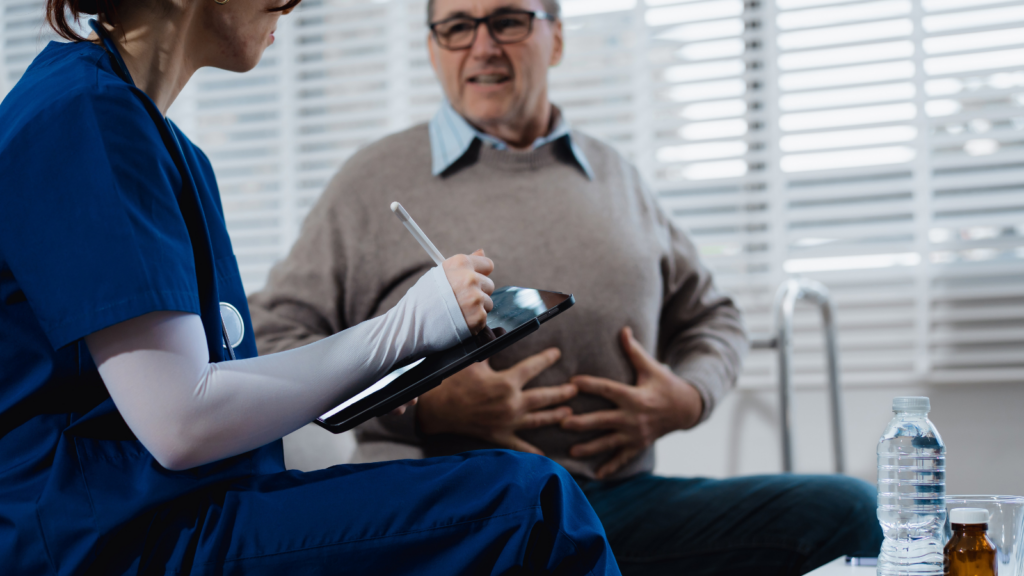 Man holds his chest in a medical appointment, a doctor in scrubs writes notes on an ipad